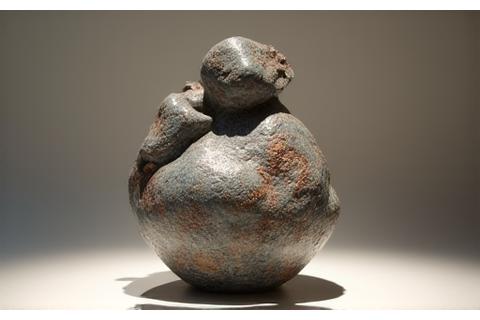 Abstract handcrafted stoneware art piece with rough texture and unique glazing, displayed in a gallery setting.
