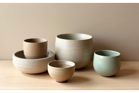 Assortment of handmade sustainable stoneware mugs and bowls in warm, earthy tones.
